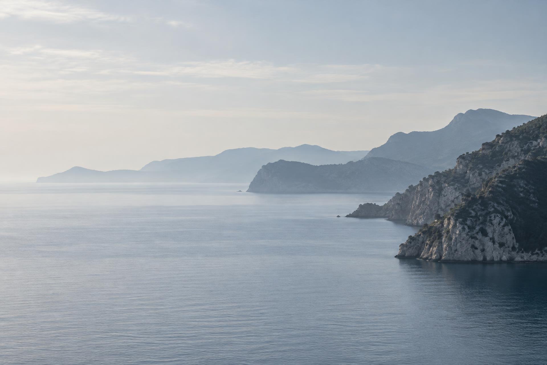 Calm Mediterranean horizon with layered Riviera headlands fading into cool morning haze